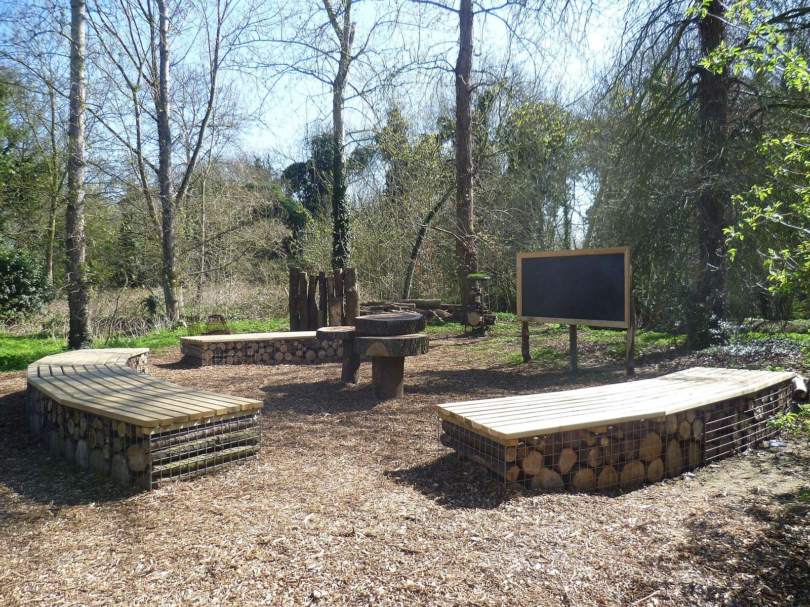 Crane Park outdoor classroom: log-filled curved benches, stump table, blackboard
