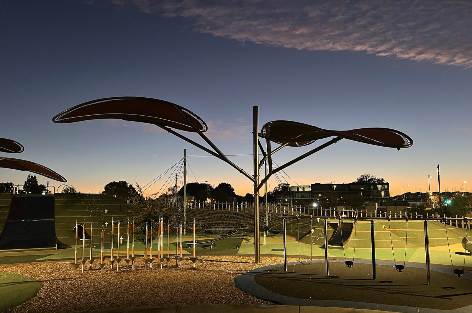 Margaret Mahy Family Playground at dusk: swing bay, balance poles and net