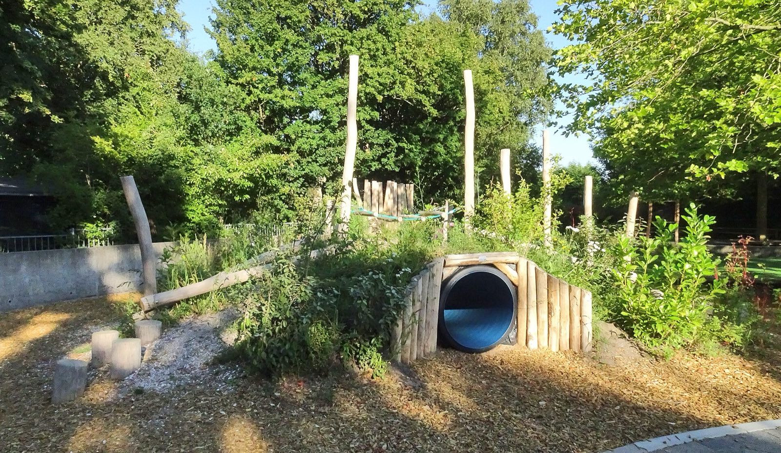 Schoolyard nature-play mound with culvert tunnel and log posts, Netherlands