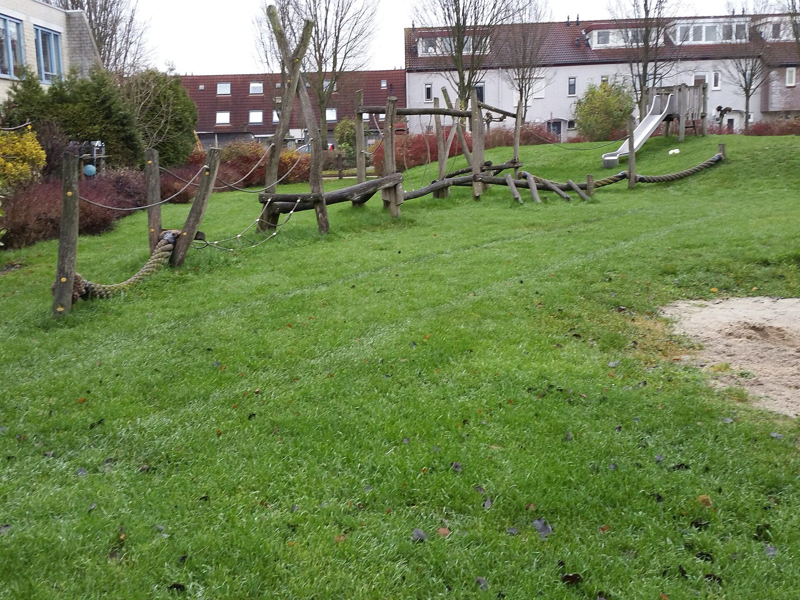 Log and rope play route on a grassed mound with slide, Netherlands