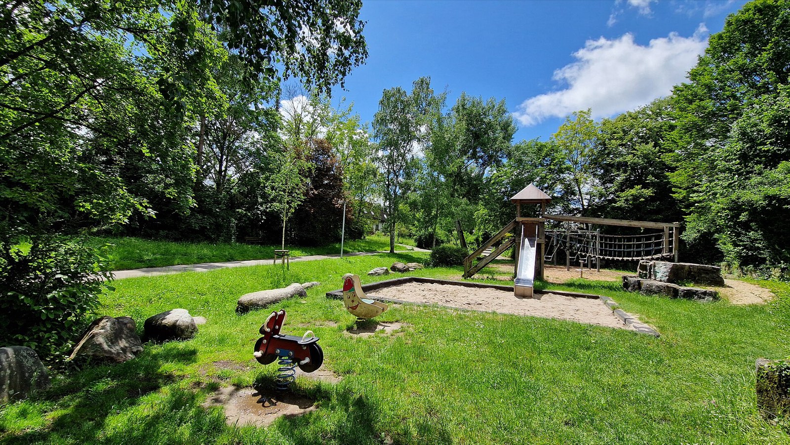 Sannentalstrasse playground: Sand play area beside a stream, ringed by trees